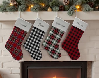 May include: Four Christmas stockings hanging in a row, each featuring a white cuff embroidered with the names Isabel, Josh, Cameron, and Charity. The stockings display various plaid and buffalo check patterns in red, black, white, and green.