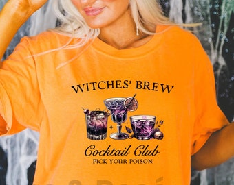 May include: Orange t-shirt with the text "WITCHES' BREW" and "Cocktail Club PICK YOUR POISON" with a graphic of three purple cocktails. The text "Bubbles & Rosé" is at the bottom of the shirt in a smaller font. The shirt is on a model wearing a black beanie.