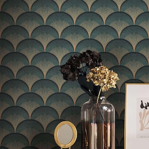 May include: A decorative wall with a teal and gold fan pattern. A clear glass vase holds dark and gold dried flowers. A small gold mirror and framed art piece sit on a black surface.