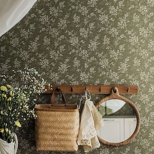 May include: A wooden wall-mounted rack with hooks and a round wooden mirror hanging on a green floral wallpaper. A woven basket with a leather handle and a white lace doily are hanging on the hooks.