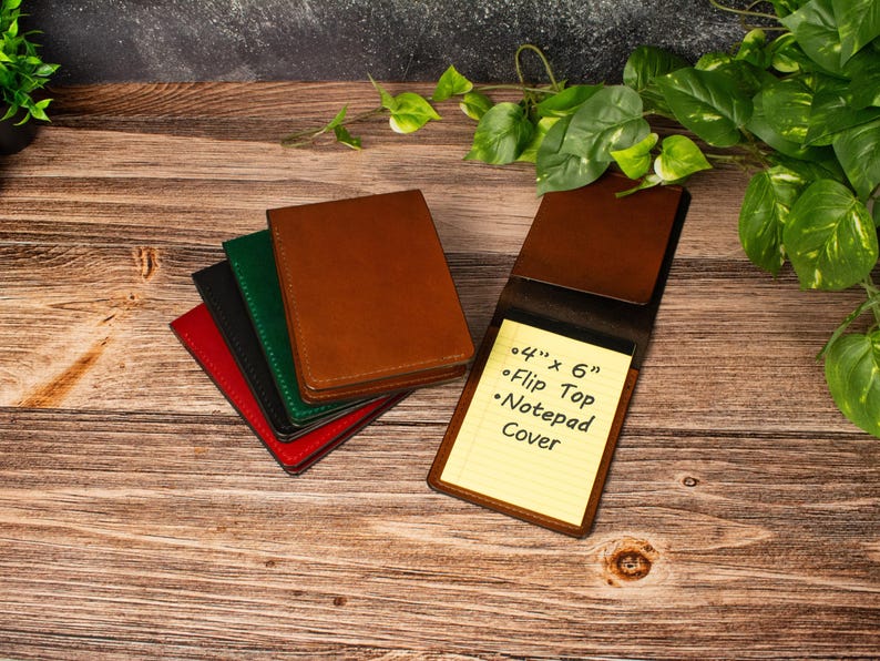 May include: A stack of four rectangular leather notepad covers in red, black, green, and brown, with one brown cover open to reveal a yellow lined notepad. The notepad features the printed text: 4" x 6" Flip Top Notepad Cover.