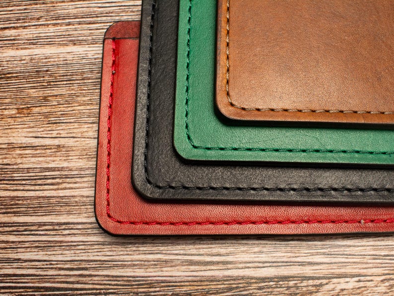 May include: A stack of four rectangular leather card holders in red, black, green, and brown, each featuring rounded corners and visible perimeter stitching in a matching thread color, layered neatly to display the edges of each individual piece.