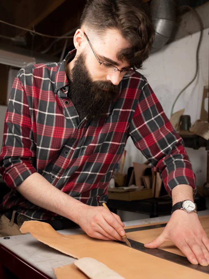 Connor Rademaker, the craftsman, cutting leather for a project in his workshop.