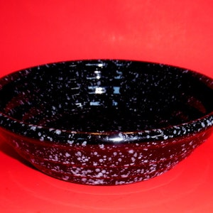 May include: A black ceramic bowl with white speckles. The bowl has a rounded shape and a slightly flared rim.