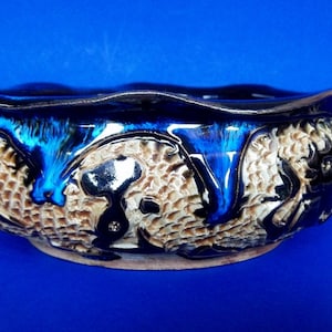 May include: A ceramic bowl with a blue and black glaze. The bowl has a textured surface and a wavy rim.