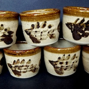 May include: Set of seven brown and white ceramic mugs with a brown fish design. The mugs are stacked in a pyramid shape.