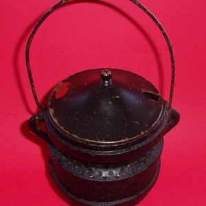 May include: Black cast iron pot with a lid and a wire handle. The pot has a textured surface and a small spout on the lid.