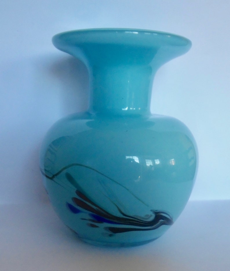 Peut inclure: Un vase en verre bleu clair avec une large ouverture et un motif tourbillonnant de noir, bleu et vert.