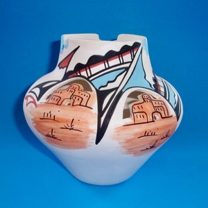 May include: White ceramic pot with cut-out designs. The pot is decorated with brown, blue, and black paint. The design features geometric shapes and stylized buildings.