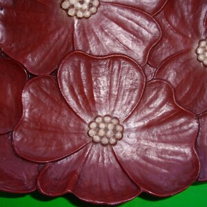 Op de afbeelding: Een decoratief bord van donkerrode klei met een reli&euml;fdesign van vijf gestileerde bloemen. De bloemen hebben witte centra met een reli&euml;f stippenpatroon.