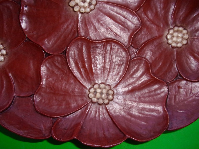 Op de afbeelding: Een decoratief bord van donkerrode klei met een reli&euml;fdesign van vijf gestileerde bloemen. De bloemen hebben witte centra met een reli&euml;f stippenpatroon.