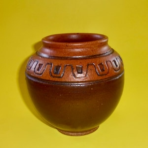 May include: A brown ceramic vase with a geometric design around the middle. The vase has a rounded body and a slightly flared lip.
