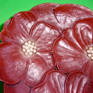 Op de afbeelding: Een close-up van een decoratieve keramische schaal in de vorm van een bloem. De schaal is diep rood van kleur met witte accenten in het midden van elke bloem.