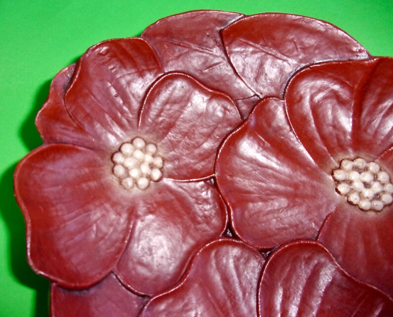 Op de afbeelding: Een close-up van een decoratieve keramische schaal in de vorm van een bloem. De schaal is diep rood van kleur met witte accenten in het midden van elke bloem.