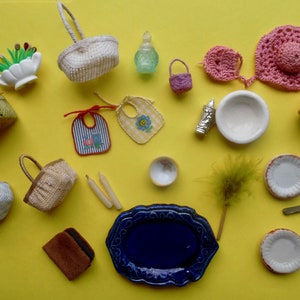 May include: A collection of miniature items on a yellow background, including baskets, a flower pot, a blue plate, a white bowl, a small bottle, a crocheted hat, a pair of bibs, a small broom, and a pair of scissors.