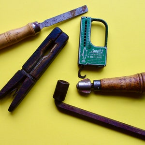 May include: A collection of vintage tools on a yellow background. The tools include a file, a clamp, a fish measuring tool, and a small awl. The fish measuring tool is green and has the text "Langley Fisherman's De-Liar" on it.