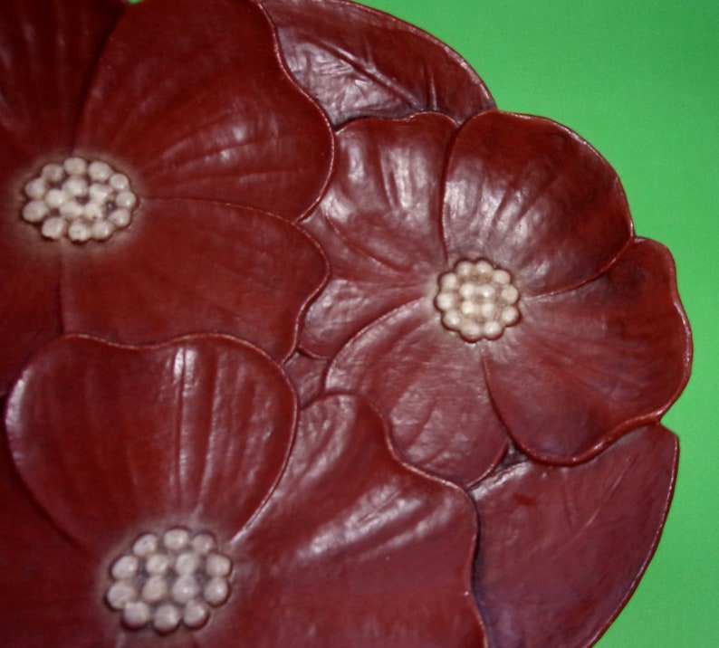 Op de afbeelding: Een decoratief bord met een bruin bloemenontwerp. Het bord heeft drie gestileerde bloemen met witte centra.