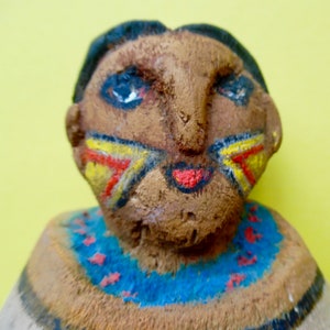 May include: A hand-painted clay figurine of a person with a red, yellow, and blue painted face and a blue and red painted necklace.