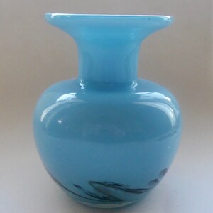 Peut inclure: Un vase en verre bleu clair avec une large ouverture et un corps arrondi. Le vase a un motif en spirale en noir et blanc.