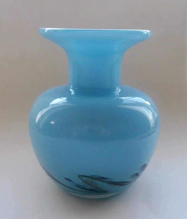 Peut inclure: Un vase en verre bleu clair avec une large ouverture et un corps arrondi. Le vase a un motif en spirale en noir et blanc.