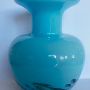 Peut inclure: Un vase en verre bleu clair avec une large ouverture et un corps arrondi. Le vase a un motif en spirale dans des tons de vert et de noir.