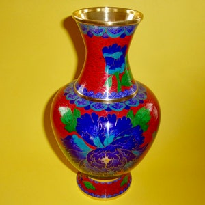 May include: A red and gold cloisonné vase with blue and green floral designs. The vase has a round body and a flared neck.