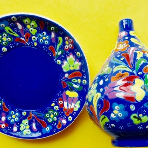 May include: A blue ceramic plate and vase with colorful floral designs. The plate has a blue center and the vase is round with a narrow neck.