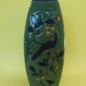 May include: A green ceramic vase with a bird and floral design. The vase is oval shaped and has a glossy finish.