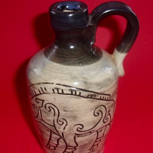 May include: A small ceramic jug with a black and white design of a stylized animal. The jug has a dark blue glaze on the top and handle.