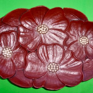 Op de afbeelding: Een decoratief dienblad van donker rood hout met een ontwerp van vier gestileerde bloemen. De bloemen hebben witte centra en zijn in een cirkelvormige opstelling gerangschikt.