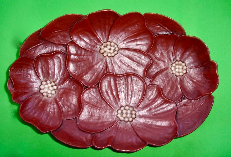 Op de afbeelding: Een decoratief dienblad van donker rood hout met een ontwerp van vier gestileerde bloemen. De bloemen hebben witte centra en zijn in een cirkelvormige opstelling gerangschikt.