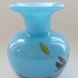 Peut inclure: Un vase en verre bleu clair avec une large ouverture et un corps arrondi. Le vase a un motif en spirale avec des accents verts, bleus et rouges.