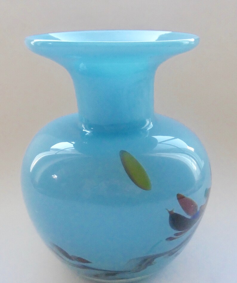Peut inclure: Un vase en verre bleu clair avec une large ouverture et un corps arrondi. Le vase a un motif en spirale avec des accents verts, bleus et rouges.