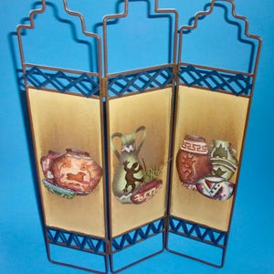 May include: A three-panel room divider made of metal with a brown finish. Each panel features a different design of Southwestern-style pottery with a tan background.