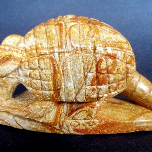 May include: A hand-carved armadillo sculpture made of brown and white stone. The armadillo is curled up in a defensive position, with its shell covering its body. The sculpture is detailed and realistic, with intricate carvings of the armadillo's scales and claws.