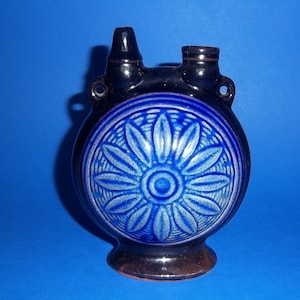 May include: A blue and brown ceramic bottle with a floral design. The bottle has two spouts and a round base.