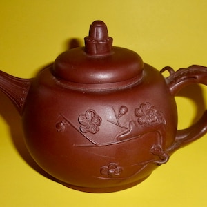 May include: A brown ceramic teapot with a lid and a handle. The teapot is decorated with a floral design.