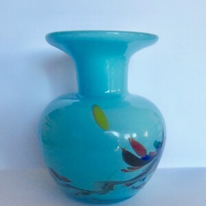 Peut inclure: Un petit vase en verre bleu clair avec une large ouverture et un corps rond. Le vase a un motif en spirale avec des &eacute;claboussures de jaune, rouge et bleu.