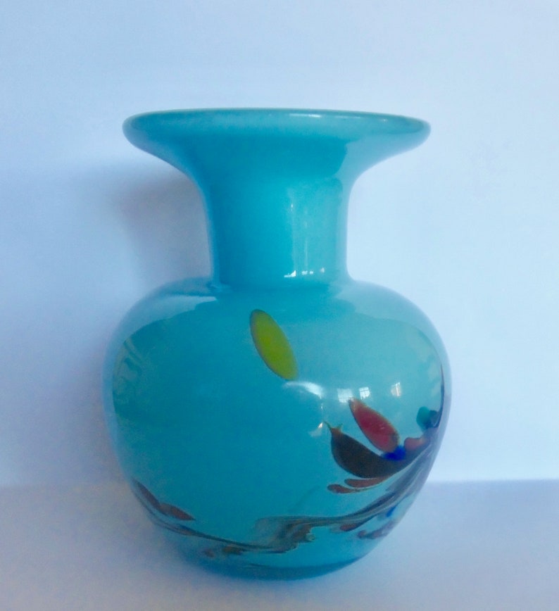 Peut inclure: Un petit vase en verre bleu clair avec une large ouverture et un corps rond. Le vase a un motif en spirale avec des &eacute;claboussures de jaune, rouge et bleu.