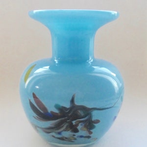 Peut inclure: Un vase en verre bleu clair avec une large ouverture et un corps rond. Le vase pr&eacute;sente un motif tourbillonnant de noir, brun, bleu, vert et jaune.