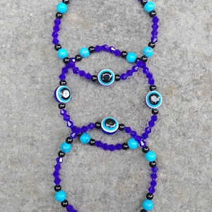 May include: Three layered bracelets with purple and black beads and blue evil eye charms.