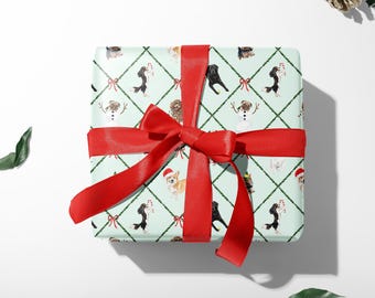Op de afbeelding: Een groen en wit cadeaupapier met een herhalend patroon van honden die kerstmanmutsen dragen, snoepstokken vasthouden en verkleed zijn als sneeuwpoppen. Het cadeau is vastgebonden met een rood satijnen lint.