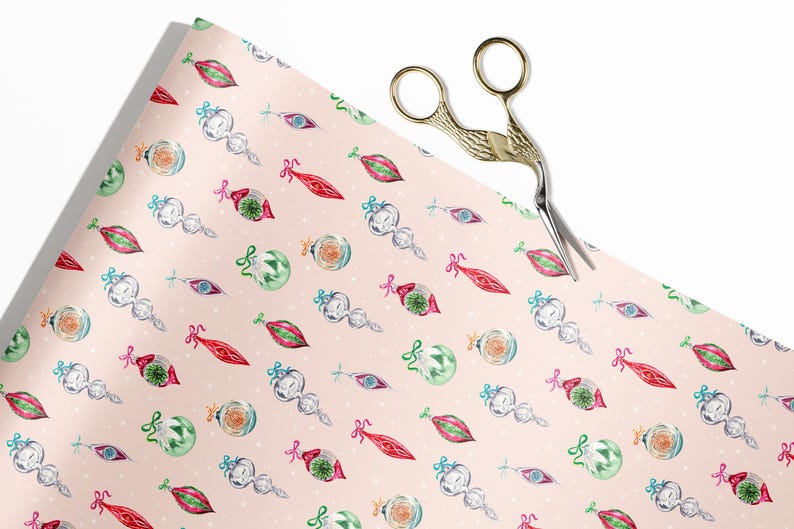 Op de afbeelding: Roze cadeaupapier met een herhalend patroon van vintage kerstversiering. De ornamenten zijn in verschillende kleuren en vormen, waaronder rood, groen, blauw en wit. Het papier is versierd met witte stippen.
