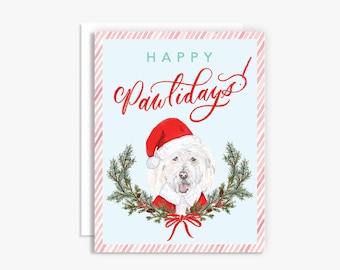 May include: A Christmas card featuring a white dog wearing a Santa hat and a red suit. The dog is surrounded by a green wreath with red berries. The text "Happy Pawlidays!" is written in red cursive on a light blue background.