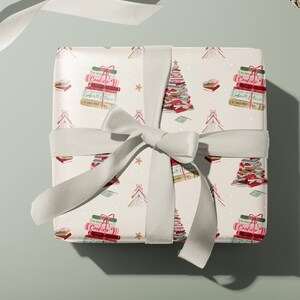 May include: A white gift box with a white ribbon tied around it. The box is wrapped in paper with a pattern of Christmas trees made of stacked books. The trees are decorated with red and pink ornaments and gold stars. The text "Cookies" is visible on the books.