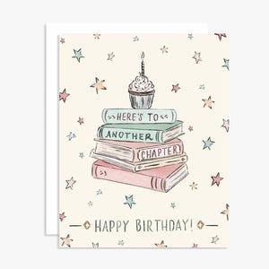 May include: A birthday greeting card with a stack of books topped with a cupcake and candle. The card has a cream background with scattered stars and the words "Here's to Another Chapter" and "Happy Birthday!"