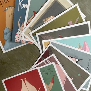 Pode incluir: Uma coleção de postais ilustrados com figuras caprichosas e texto. Os cartões exibem várias cores, incluindo vermelho, azul e verde, com desenhos em estilo cartoon. Alguns cartões têm texto como "Kon" e "Hui!"