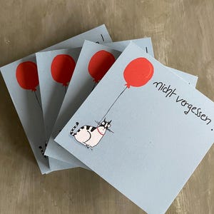 Peut inclure: Plusieurs cartes carrées bleu clair avec un ballon rouge. Un chat de dessin animé avec un collier rose est attaché à un ballon. La phrase allemande "nicht vergessen" est écrite sur une carte.