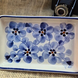 Op de afbeelding: Een rechthoekige, witte keramische bakvorm met een blauw en wit bloemenpatroon. De bloemen hebben bruine centra.