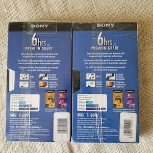 May include: Two blue and white VHS video cassette tapes with the Sony logo and the text "6hrs Premium Grade". The tapes are labeled with recording time, modes, and other features. The back of the tapes show a barcode and the text "Sony. Our media is your memory."